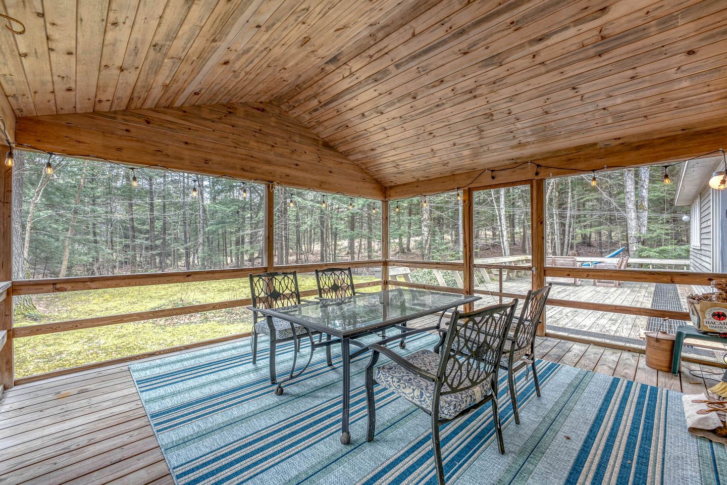 Une terrasse en bois couverte, avec une table et des chaises en verre, et offrant une vue sur la forêt environnante.