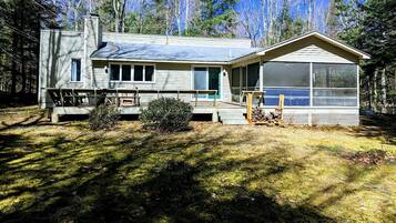 A two-story cabin with a porch, a screened porch, and a large window.