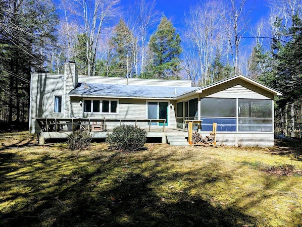 Une cabane à deux étages dotée d’une véranda, d’une terrasse grillagée et d’une grande fenêtre.