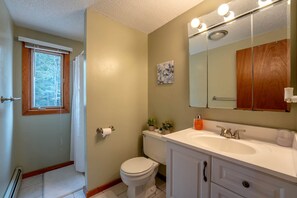 A bathroom with a toilet, sink, mirror, and a window with blinds.
