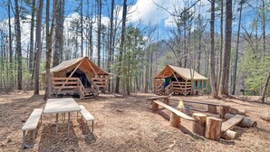 Dos cabañas de madera con bancos de madera y un brasero en un bosque.