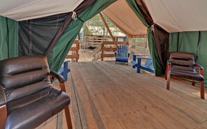 A tented outdoor area with wooden flooring, two leather chairs, and blue Adirondack chairs. - Safari Tent Bliss for You and Your Best Friend: Pet-Friendly Glamping in Suches, Georgia (Suches)