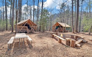 Dos cabañas de madera con bancos de madera y un brasero en un bosque.