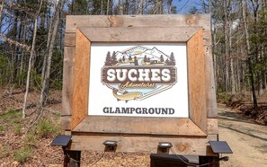 Un panneau en bois portant le logo et le texte « SUCHES Adventures GLAMPGROUND ».