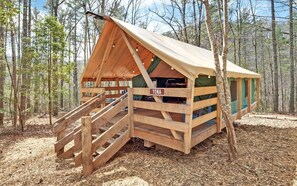Una cabaña de madera con una rampa que conduce a la entrada, con la leyenda 'YONA', rodeada de un bosque.