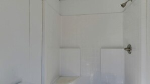 Un baño con paredes de azulejos blancos, una zona de ducha y un inodoro.