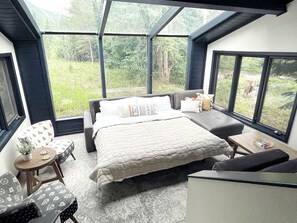 A bedroom with a bed, seating area, and large windows. - Luxury A-Frame with Hot Tub for Dreamy Vacations in Colorado (Blue River)
