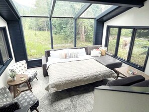 A bedroom with a bed, seating area, and large windows. - Luxury A-Frame with Hot Tub for Dreamy Vacations in Colorado (Blue River)
