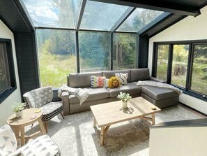 A modern living room with a glass ceiling, a sectional sofa, a round coffee table, and a small side table with a plant. - Luxury A-Frame with Hot Tub for Dreamy Vacations in Colorado (Blue River)