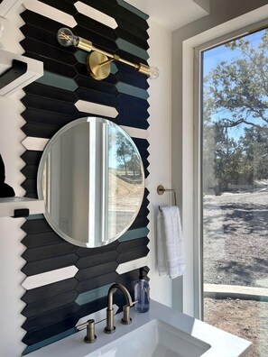 A bathroom with a modern design, featuring a large mirror, a sink, and a faucet. - Luxurious Cabin Perfect for a Romantic Escape in Wimberley, Texas (Wimberley)