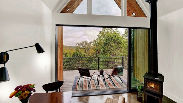 Um interior moderno com uma grande porta de vidro deslizante que dá para um deck externo, uma lareira preta e uma sala de jantar com mesa e cadeiras.