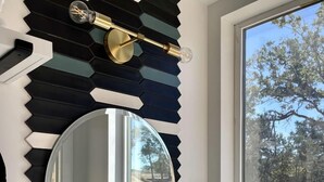 Casa de banho com design moderno, apresentando um espelho grande, uma pia e uma torneira.
