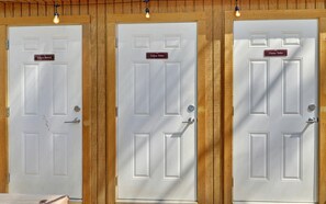 Three white doors with wooden frames and labels indicating 'Unisex Shower' and 'Unisex Toilet'. - Discover the Best Glamping in Georgia with a Stay in This Safari Tent (Suches)