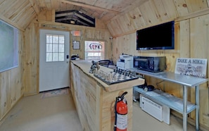 Interior de una cabaña de madera con cocina, una puerta, extintor, televisor y un letrero que dice 'TAKE A HIK!'