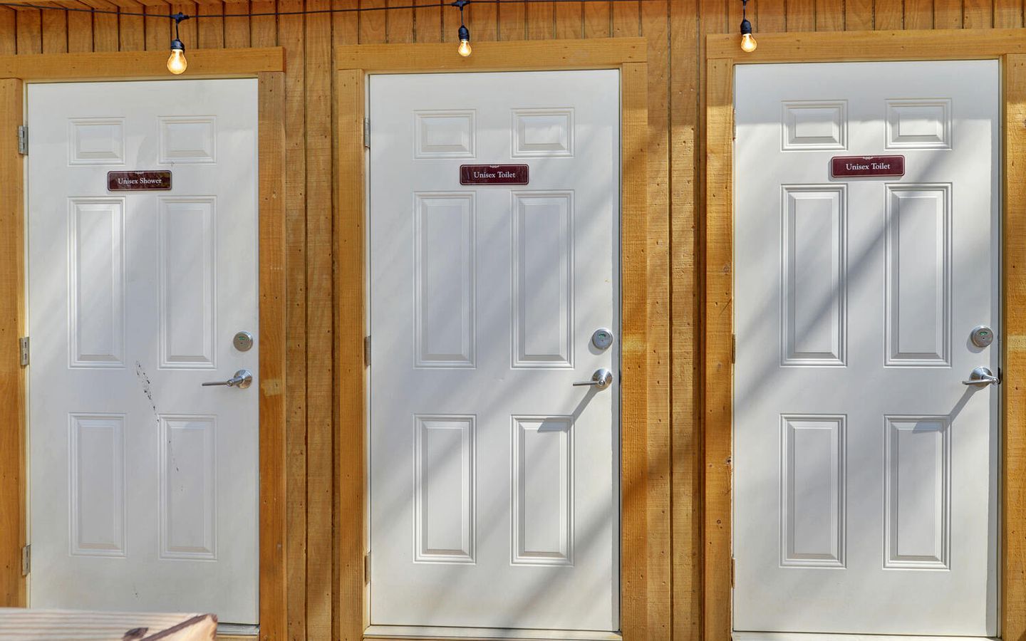 Three white doors with wooden frames and labels indicating 'Unisex Shower' and 'Unisex Toilet'.