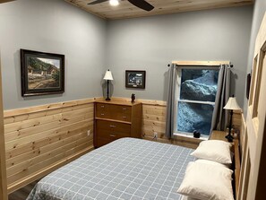 Une chambre à coucher comprenant un lit, une tête de lit en bois, une commode, une fenêtre avec des rideaux et des lampes fixées au mur.