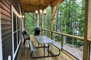 Une terrasse extérieure couverte, dotée d’une table de pique-nique et de chaises, entourée d’une rambarde en bois et offrant une vue sur une zone boisée.