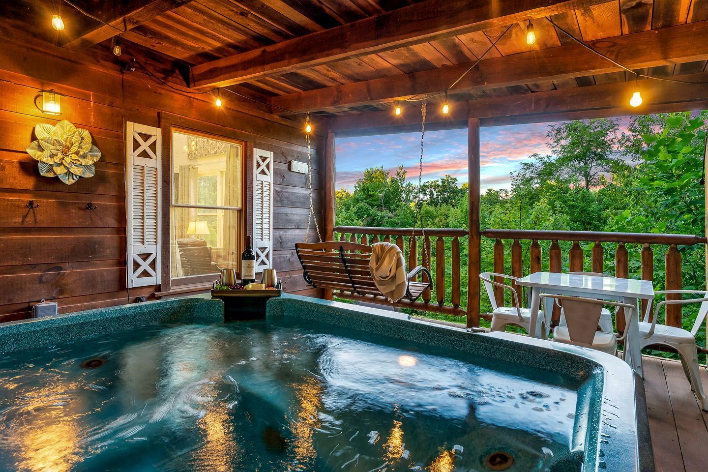 Een houten terras met een jacuzzi, zitplaatsen buiten en uitzicht op bomen.