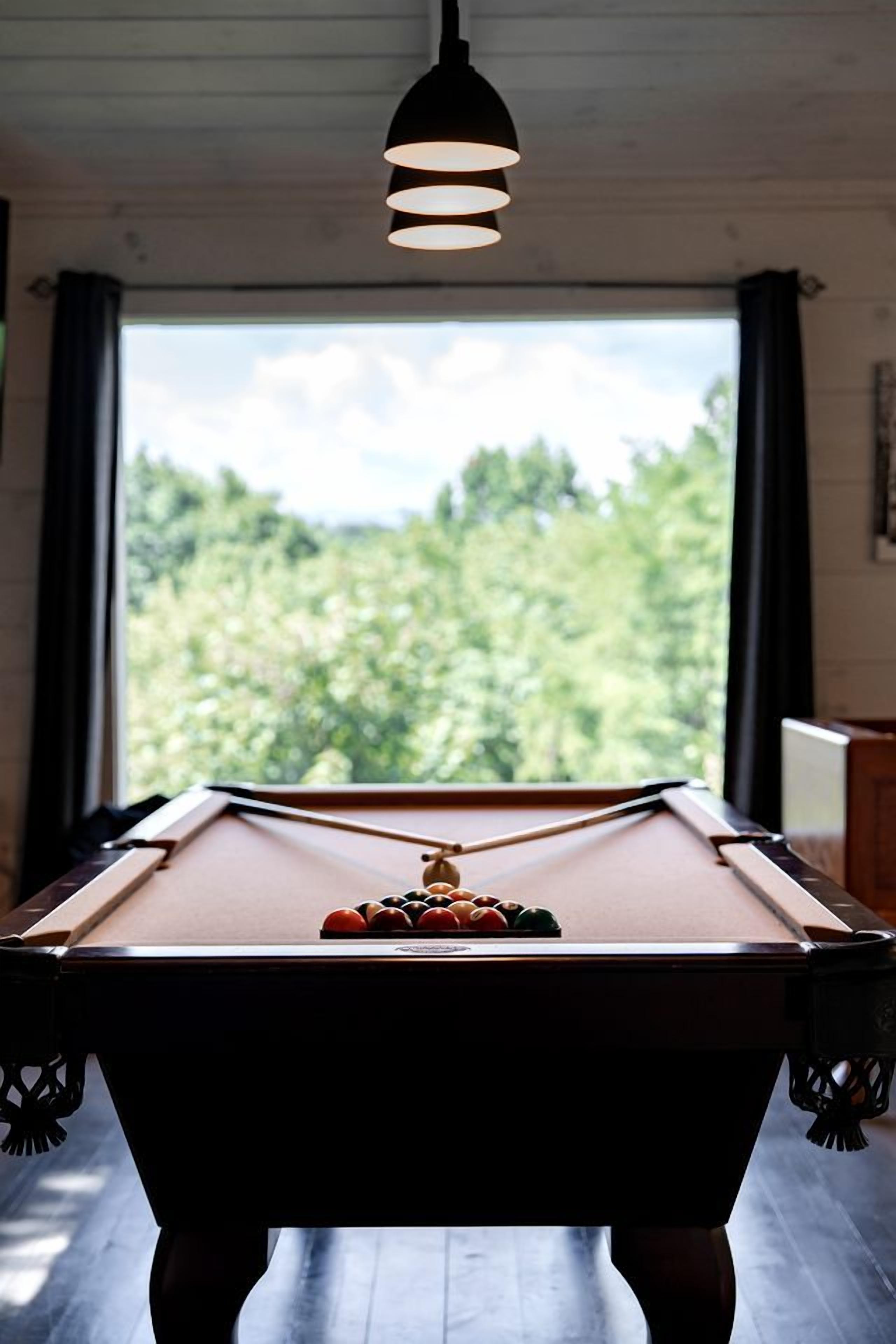 Ein Billardtisch mit Blick auf einen Wald durch ein Fenster.