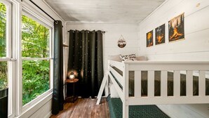 Une pièce chaleureuse avec un lit superposé, une petite table avec une lanterne et une vue sur la verdure.