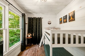 A cozy room with a bunk bed, a small table with a lantern, and a view of greenery outside. - Gorgeous Secluded Wooden Cabin with Hot-tub and Pool Table in Sevierville, Tennessee (Sevierville)