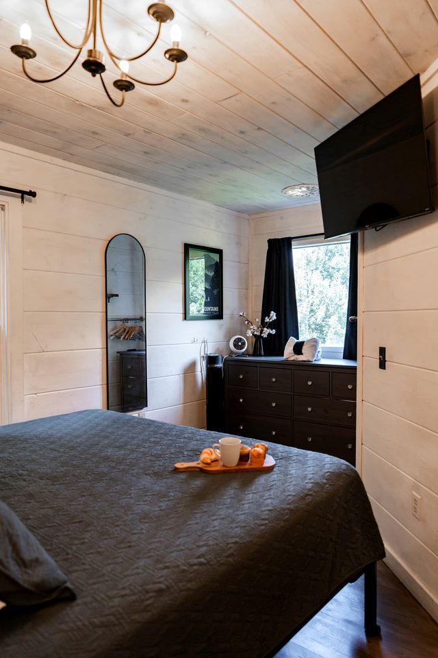 Un dormitorio con cama, cómoda, televisor y ventana con cortinas.