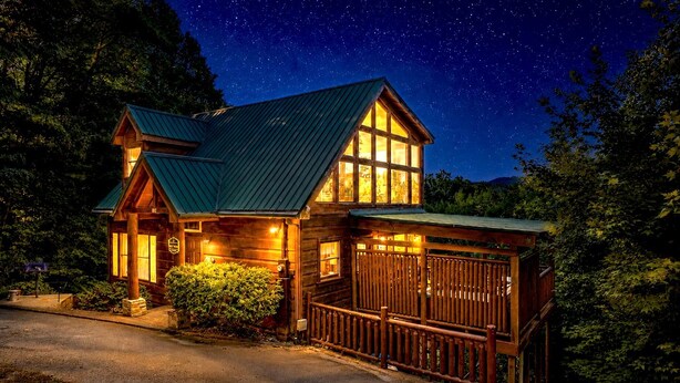 Une cabane en bois avec un toit en métal, de grandes fenêtres et une véranda entourée d’une clôture.
