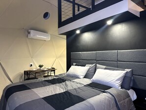 Ein modernes Schlafzimmer mit einem großen Bett, einem kleinen Tisch mit Lampe und einer Wand-Klimaanlage.