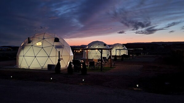 Geodesic dome structures with seating and tables, set against a twilight sky.