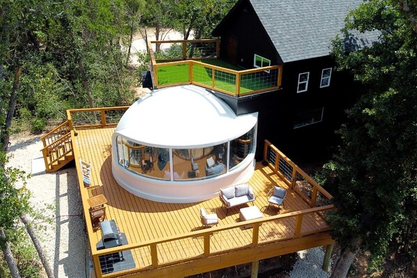 A circular building with a glass dome, a deck with seating, and a black house nearby.