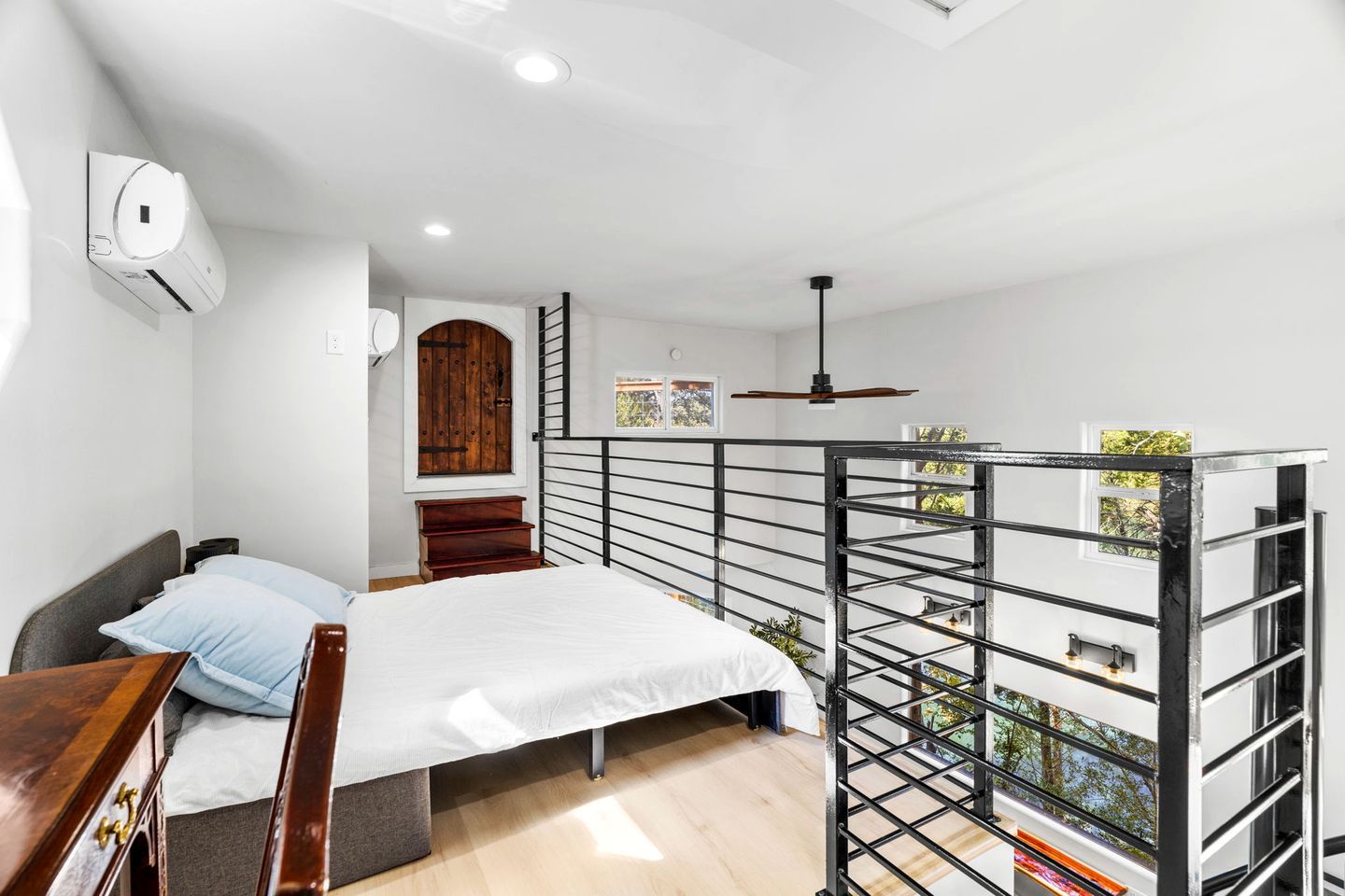 A bedroom with a bed, a desk, a wardrobe, a window, and a balcony with a railing.
