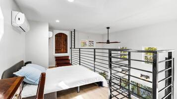 Quarto com cama, escrivaninha, guarda-roupa, janela e varanda com grade.