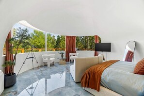 A modern room with a bed, a sofa, a small table, a tripod, and a TV.