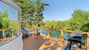 A deck with outdoor furniture, a grill, and a view of trees and water.