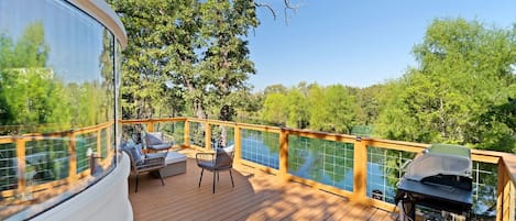 A deck with outdoor furniture, a grill, and a view of trees and water.