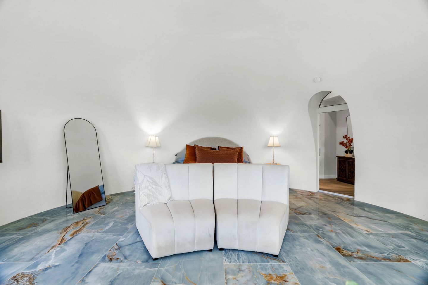 Een kamer met een witte bank, twee lampen, een spiegel en een marmeren vloer.