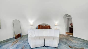 Een kamer met een witte bank, twee lampen, een spiegel en een marmeren vloer.