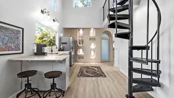 Cozinha moderna com ilha central, banquetas, escada em espiral e vista para o exterior.