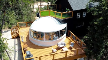 Um edifício circular com uma cúpula de vidro, um terraço com assentos e uma casa preta nas proximidades.