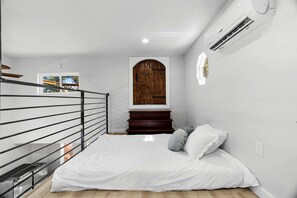 Une chambre à coucher avec un lit, une porte en bois, un escalier et un appareil de climatisation.