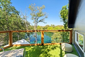 Un balcon offrant une vue sur un lac d’un bleu limpide, entouré d’arbres et d’une pelouse agrémentée de mobilier d’extérieur.