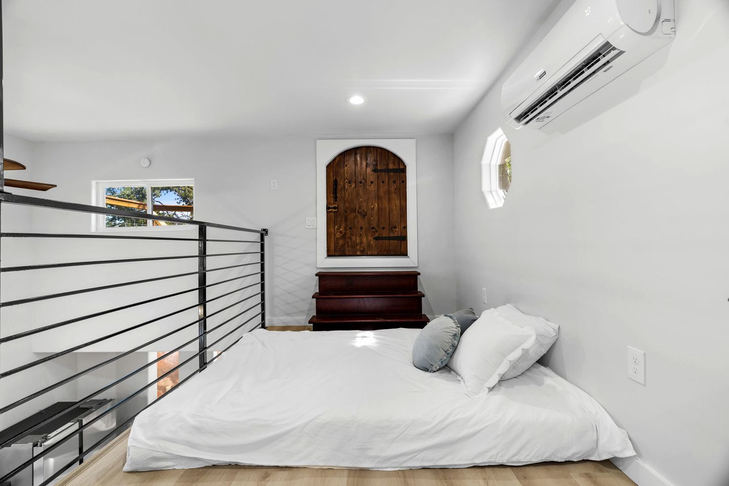 A bedroom with a bed, a wooden door, a staircase, and an air conditioning unit.
