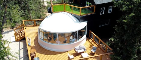 Un edificio circular con una cúpula de vidrio, una terraza con asientos y una casa negra cerca.