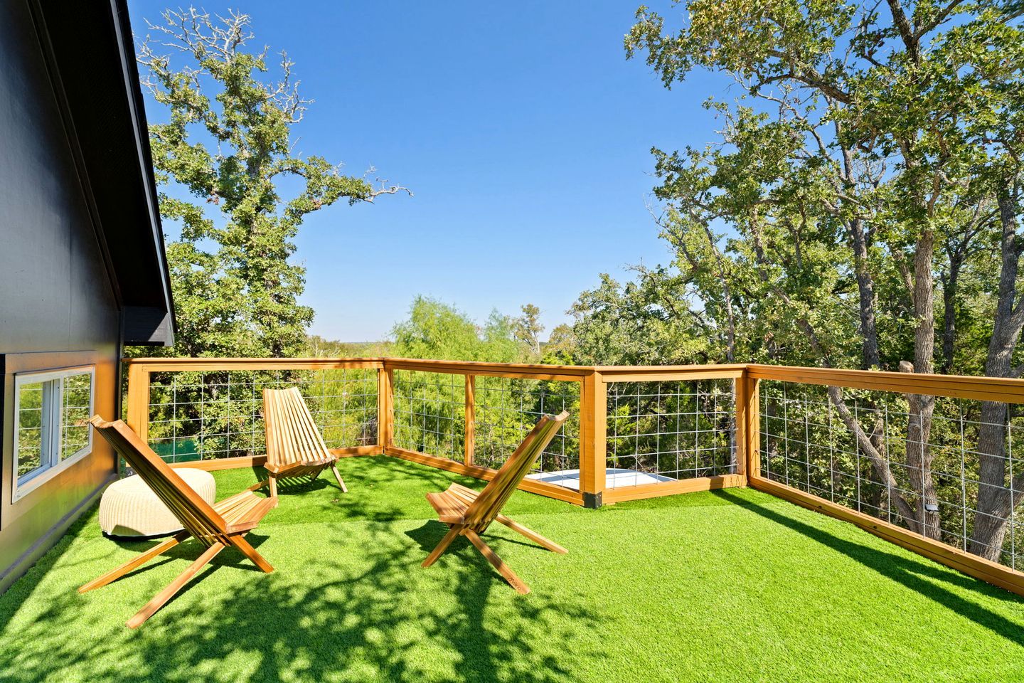 A balcony with artificial grass, wooden furniture, and a view of trees.