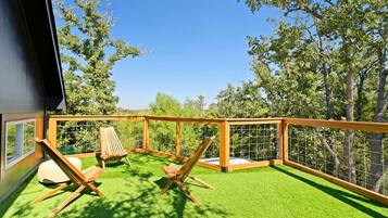 A balcony with artificial grass, wooden furniture, and a view of trees.