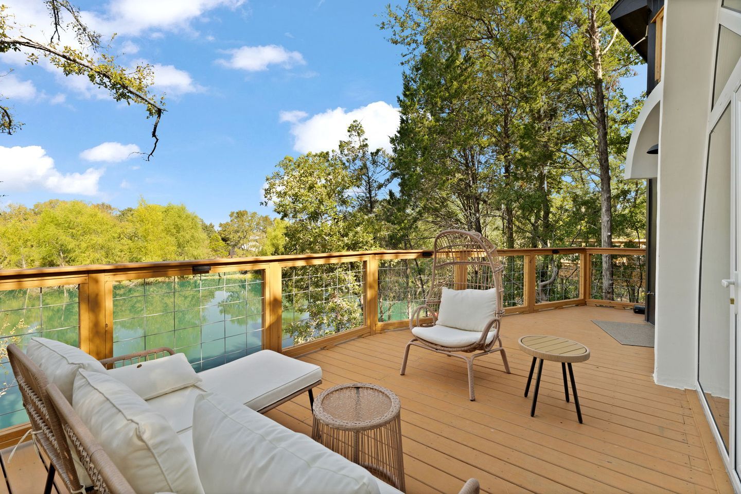 A deck with a glass balustrade, wicker furniture, and a view of trees and water.