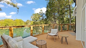 A deck with a glass balustrade, wicker furniture, and a view of trees and water.