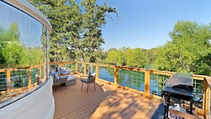 A deck with outdoor furniture, a grill, and a view of trees and water.