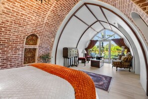 Une chambre avec un grand lit, un mur en briques, une fenêtre et une vue sur l’extérieur.