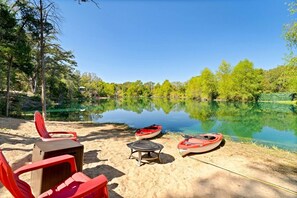 Un cadre idyllique au bord du lac, avec une chaise rouge, une petite table et deux kayaks à proximité de l’eau.